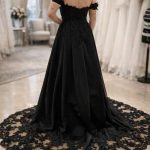 Rückenansicht eines schwarzen Brautkleids mit langer Schleppe, kunstvoller Spitze am Saum und Off-Shoulder-Schnitt.